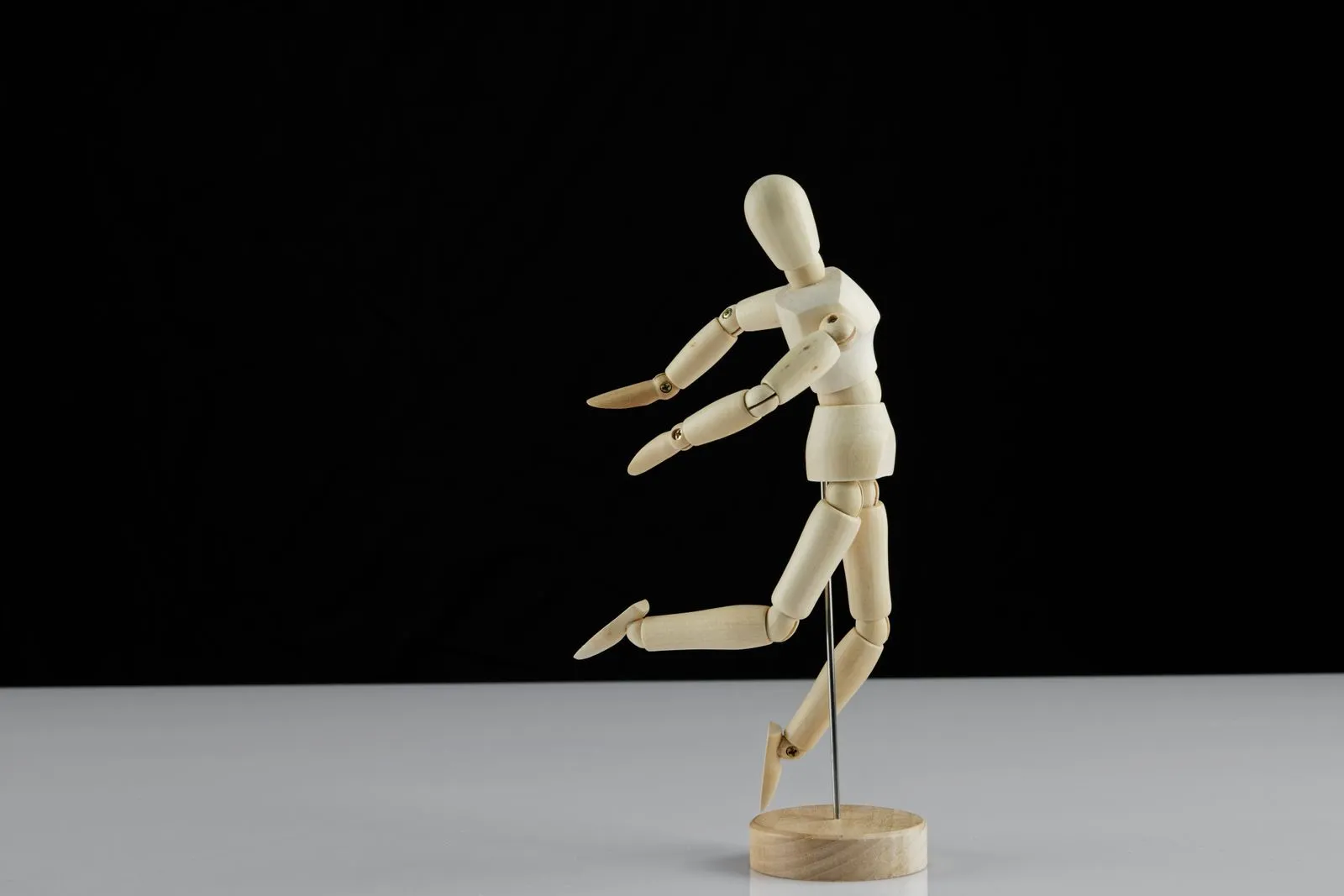 Wooden mannequin figurine captured mid-motion against black background.